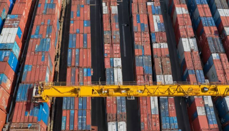 Luftaufnahme von gestapelten Schiffscontainern mit einem gelben Kran, der sie überquert. Dies spiegelt den wachsenden Fokus auf ESG und nachhaltige Lieferketten in Deutschland wider.
